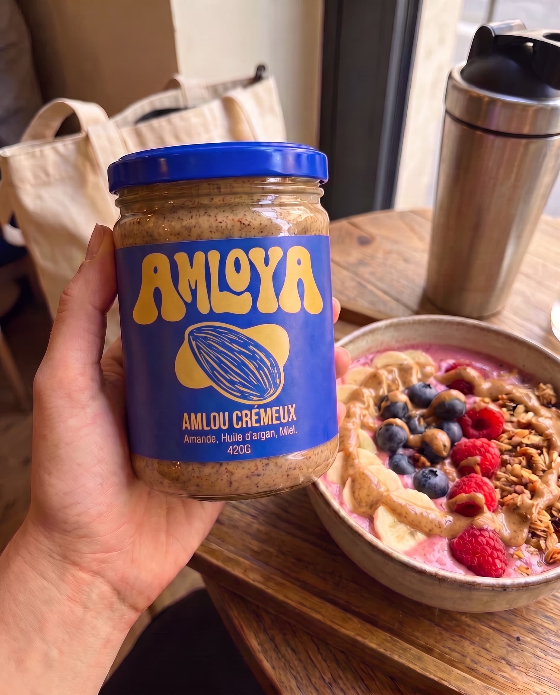 Main tenant le pot AMLOYA au-dessus d'un smoothie bowl à l'amlou